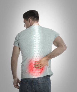 Man suffering from pain in spine on grey background clipart
