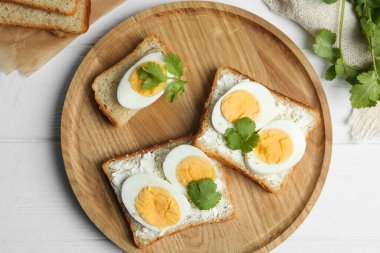 Beyaz ahşap masada servis edilen haşlanmış yumurtalı lezzetli sandviçler.