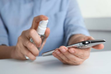 Beyaz masadaki akıllı telefona antiseptik sıkan bir kadın.