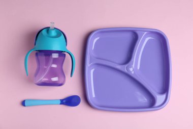 Açık pembe arka planda renkli plastik bulaşık takımı, düz. Bebek maması servisi.