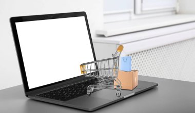 İnternetten alışveriş. Masada küçük el arabası ve çantaları olan modern bir laptop.