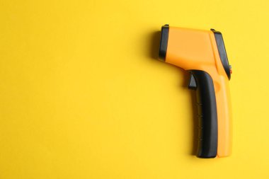 Sarı arka planda modern temas olmayan kızılötesi termometre, üst görüş. Metin için boşluk