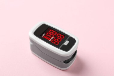 Pembe arka planda modern parmak ucu nabız oksimetresi, yakın plan.