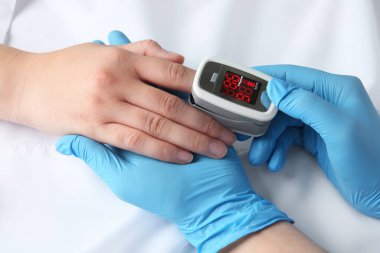 Doktor, modern parmak uçlu hastayı muayene ediyor. Nabız oksimetresi yatakta, yakın plan.