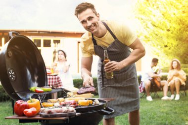Barbekü ızgarasında bira pişiren genç adam.