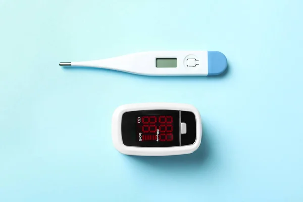 現代の指先パルス酸素濃度計とライトブルーの背景のデジタル温度計 フラットレイ — ストック写真