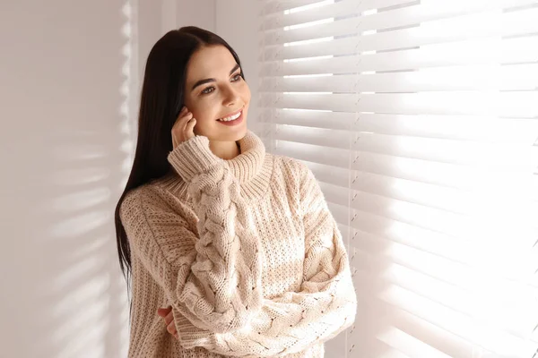 年轻女人穿着暖和的毛衣在家里靠窗的地方 — 图库照片