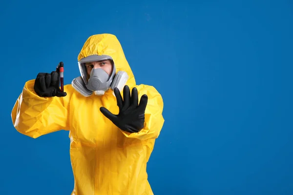 身穿化学防护服的男子拿着蓝色背景的血样试管 空白处有文字 病毒研究 — 图库照片