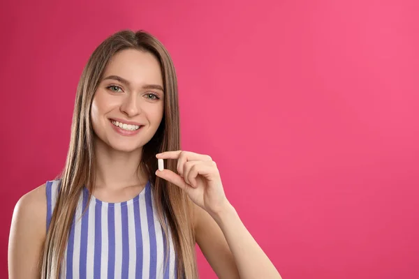 Young woman with vitamin pill on pink background. Space for text