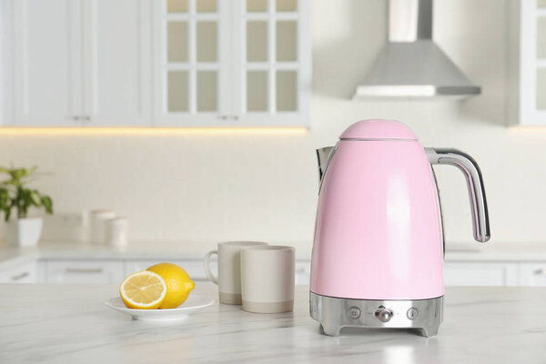 Modern electric kettle, cups and lemons on table in kitchen