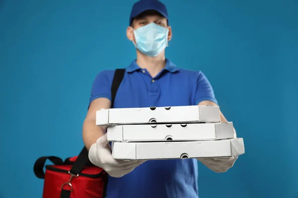 青い背景にピザボックスを保持保護マスクと手袋で宅配便 コロナウイルス隔離中の食品配送サービス — ストック写真
