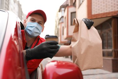 Koruyucu maskeli ve eldivenli bir kurye açık hava arabasının camından emir veriyor. Coronavirus karantinası sırasında teslimat servisi