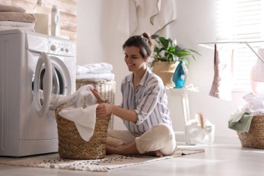 Çamaşır makinesinden çamaşırları çıkaran genç bir kadın.