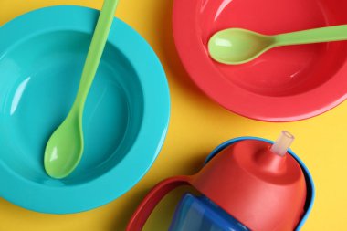 Sarı arka planda renkli plastik bulaşık takımı, düz. Bebek maması servisi.
