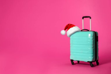 Pembe arka planda Noel Baba şapkası olan şık bir bavul, mesaj için yer. Noel tatili 