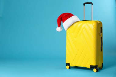 Mavi arka planda Noel Baba şapkası olan şık bir bavul. Mesaj için yer var. Noel tatili 