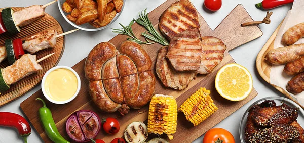 Flat lay composition with barbecued meat and vegetables on light table. Banner design