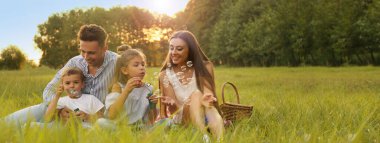 Mutlu aile piknik yapıyor ve gün batımında parkta sabun köpüğü üflüyor. Mesaj için yer var. Pankart tasarımı