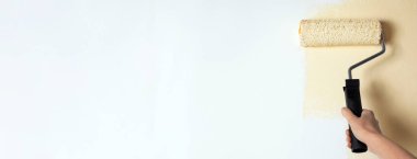 Profesyonel dekoratör bej boyalı beyaz duvarı boyuyor, yazı için yer var. Pankart tasarımı