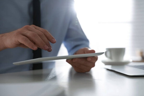 Businessman working with modern tablet at white table in office, closeup