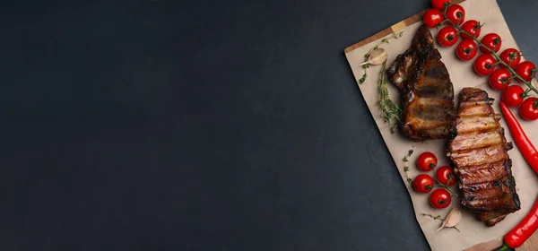 Serving board with tasty grilled ribs and space for text on black table, top view. Banner design