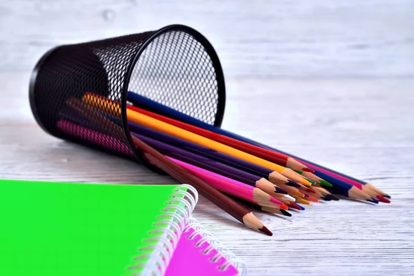 Color pads and colored pencils in a container on an aged white background