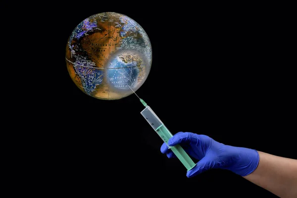 Planet earth infected with a virus, a hand in a medical glove with a syringe makes an injection, covid-19, the virus close-up black background copyspace