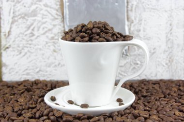 Bir fincan ve tabak koyu kavrulmuş kahve çekirdekleri