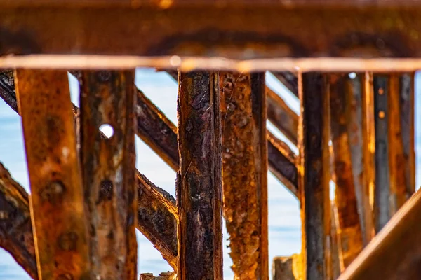 Very rusty metal frames, old thick metal subject to corrosion from salty seawater. Red bright color in sunlight