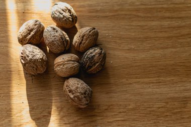 Katı ve kabartmalı kahverengi kabuklu cevizler, sert güneş ışığıyla aydınlatılmış, ahşap bir masanın üzerinde yatıyor.