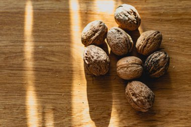 Katı ve kabartmalı kahverengi kabuklu cevizler, sert güneş ışığıyla aydınlatılmış, ahşap bir masanın üzerinde yatıyor.