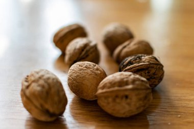 Katı ve kabartmalı kahverengi kabuklu cevizler, sert güneş ışığıyla aydınlatılmış, ahşap bir masanın üzerinde yatıyor.