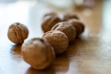 Katı ve kabartmalı kahverengi kabuklu cevizler, sert güneş ışığıyla aydınlatılmış, ahşap bir masanın üzerinde yatıyor.