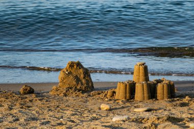 Children's sand figurines on the beach. Buildings made of water, sand and stones, illuminated by sunlight from the side, at sunset, a beautiful photo for memory