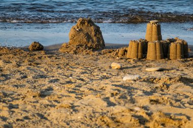 Children's sand figurines on the beach. Buildings made of water, sand and stones, illuminated by sunlight from the side, at sunset, a beautiful photo for memory