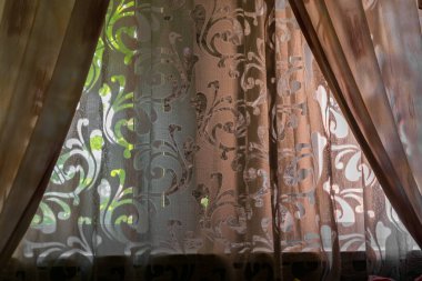 Parlak ışığın odaya girdiği büyük ve rahat bir pencere. Daire kumaşının içi. Açılış desenli renkli ve şeffaf perdeler.