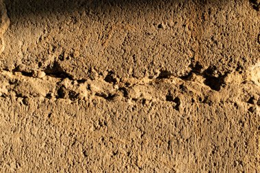 The cemented wall is grey and brown with texture and relief, the building material is old and battered in the sunlight at sunset