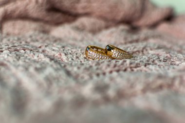 Büyük boyutlarda altın modern küpeler, tamamen küçük şeffaf taşlarla kaplı Zirkonya küpü, kadife pembe arka planda yapay altın bir parça oluşturur.