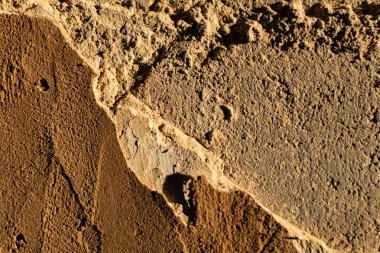 The cemented wall is grey and brown with texture and relief, the building material is old and battered in the sunlight at sunset