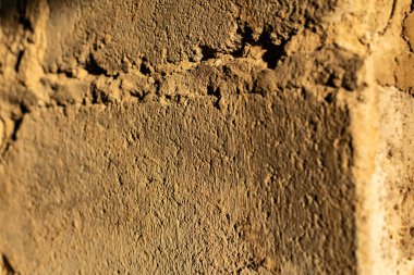 The cemented wall is grey and brown with texture and relief, the building material is old and battered in the sunlight at sunset