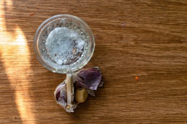 Şeffaf cam tuzluk içinde yenilebilir beyaz tuz ve kahverengi ahşap bir masa üzerinde sarı dolgulu, kabuğunda bir baş eski sarımsak