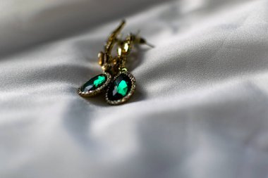 Yeşil, zümrüt taşlı metal altın küpeler, beyaz ve sarı yapay elmaslar. Düz beyaz bir arka planda. Parlak ve şenlikli bir dekorasyon.