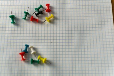 Colored small office buttons with different convenient protective hats, modern office details scattered on notebook leaves in a check