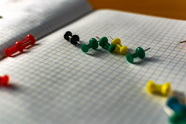 Colored small office buttons with different convenient protective hats, modern office details scattered on notebook leaves in a check