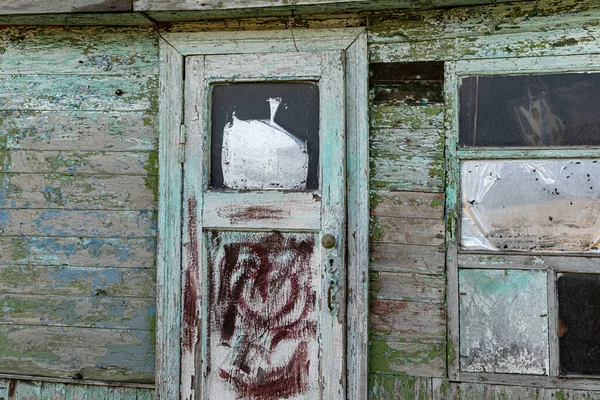 Old wooden doors on a collapsing building, a vintage barn, peeling paint, littered planks, the construction site is tilted to one side and damaged by temporary dirt