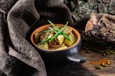 Püre ve patatesli çorba. Kavanozdan yeşil soğan ve bezelye ile süslenmiş. Kömürleşmiş ahşap bir arka planda, kumaş ve doğal dallarla seramik bir tencerede servis yapmak.