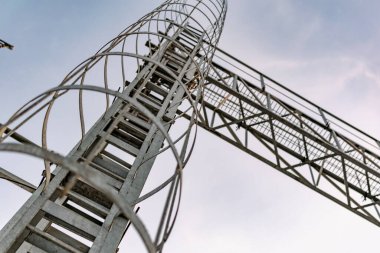 İnce ama güçlü halkalardan yapılmış metal bir yapı. Yüksek bir kulede birbirine zincirlenmiş. Gri boyayla kaplı, en tepeye çıkmak için.