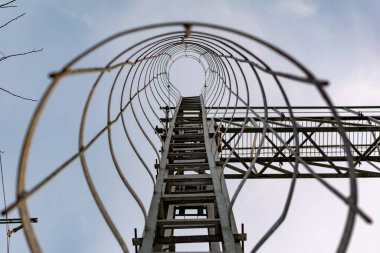 İnce ama güçlü halkalardan yapılmış metal bir yapı. Yüksek bir kulede birbirine zincirlenmiş. Gri boyayla kaplı, en tepeye çıkmak için.