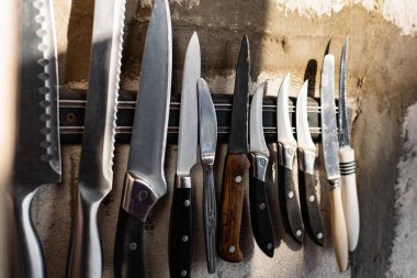 Yatay mıknatıs tutacağında asılı farklı boyutlarda ve şekillerde metal bıçaklar. Blok ve çimentodan yapılmış gri beton bir duvarda