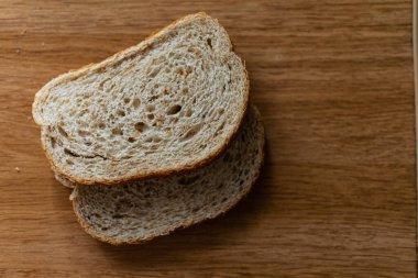 İki dilimlenmiş kepekli ekmek ve gevrek bir çavdar ekmeği. Kahverengi ahşap bir masa üzerinde uzanıyorlar. Güneş ışığında mutfakta taze piştikten sonra.